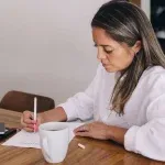 Femme entrepreneure planifiant sa rentrée avec un carnet et un café, pour préparer son business en septembre